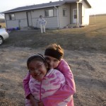 Tessa Plainfeather and Emily Moccasin embrace in front of their grandmother’s home. Tessa and her parents live with her grandmother and uncle in separate homes on the same allotment of land.