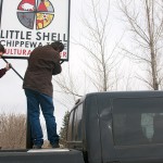 Tribal Chairman Gerald Gray and council member Clarence Sivertsen use a pickup truck as a ladder to put up the Little Shell Chippewa Tribe Cultural Center's new sign. The building was completely renovated by volunteers and will open in the summer.