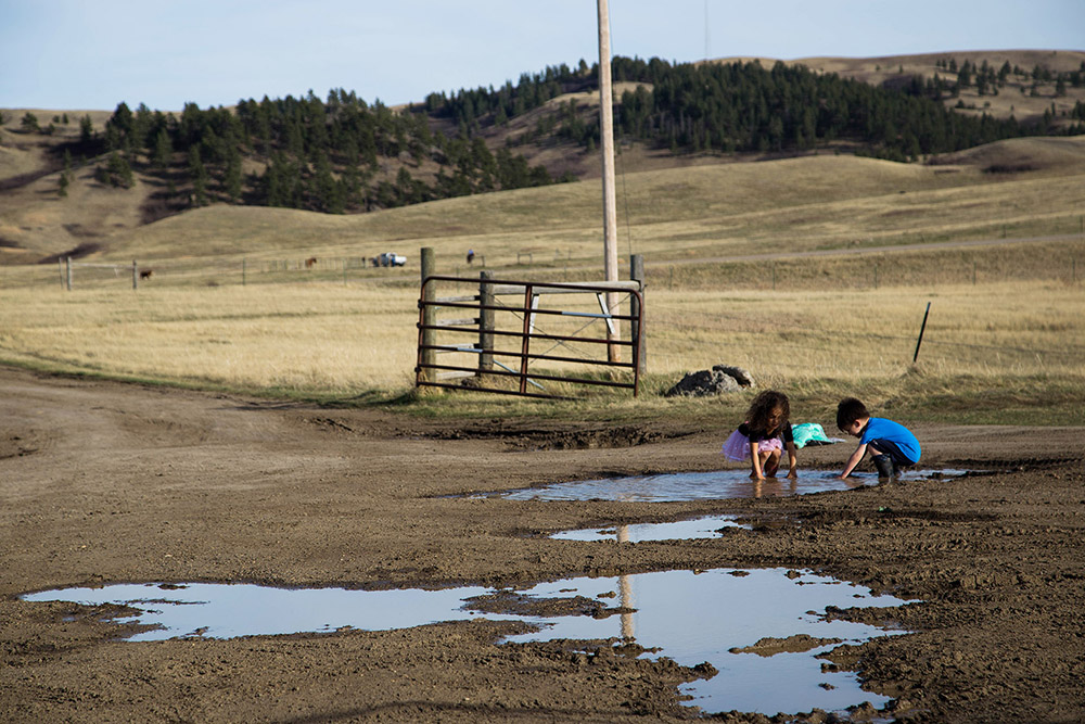 Javon Wing’s niece and nephew, Brooklyn and Tristan Montes, play in the mud outside their grandparents’ home on the Rocky Boy’s reservation.